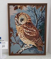 Framed cross stitch artwork featuring an owl on a branch with blue sky background.