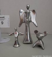 Photo showing all three Hoselton metal sculptures together on a neutral background: two angel candle holders and a stylized mouse figurine