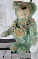 Front view showing teddy bear named Meadow with daisy flower headband and crocheted shawl, standing in front of a window.