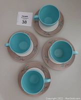 Four Melmac cups and saucers arranged from above showing turquoise blue cup interiors and taupe/salmon-colored saucers adorned with delicate floral designs.
