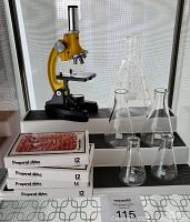 Yellow National Geographic microscope with light, four boxes of prepared slides, and five glass beakers on tiered display.