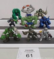 Front view of nine Marvel Super Hero Squad figures including multiple Hulk versions and other characters arranged standing on tiered white and dark gray platforms