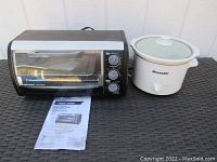 Black and Decker toaster oven and Bravetti slow cooker side by side on a textured surface with Black and Decker manual placed in front.