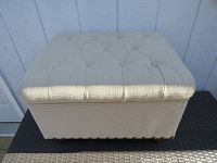 Front view of off-white tufted storage ottoman showing upholstery and button tufting on top.