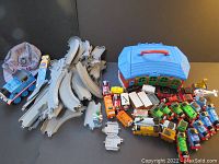 Photo showing overall contents including diecast engines, track pieces, roundhouse carrier, whistle, and conductor's hat