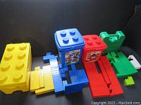 Photo showing three large LEGO Duplo storage boxes in yellow, blue, and red, alongside green base pieces.