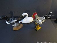 Four bird figures on a black background: loon, swan, rooster, and duck in front.