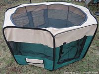 Hexagonal cat corral set up outdoors showing beige fabric upper edge and green fabric lower section with black mesh sides.