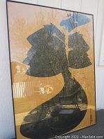 Framed poster leaning outdoors showing full image of black cape artwork on brown background.