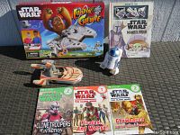 Seven Star Wars items arranged outdoors on concrete floor showing toys, game, books, and flashlight