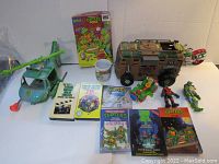 Full lot overview showing vehicles, action figures, books, VHS tapes, puzzle and mug.