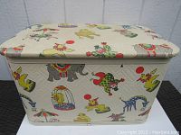 Full view of the quilted off-white hamper decorated with bright, multi-colored circus themed illustrations including elephants, clowns, and animals.