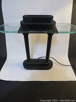 Front view of black desk lamp with two vertical cylindrical rods and clear rectangular glass top, lamp off.