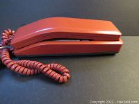 Side view of vintage red Northern Telecom Silhouette phone with coiled red cord, lying flat on a dark surface.