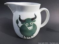Full side view of white ceramic pitcher with green cow design on black background.