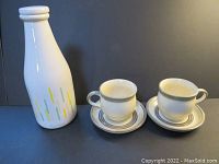 Photo showing the vintage ceramic milk bottle with two Laurentian mugs and saucers set on a black background.