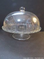 Clear glass cake stand with domed cover shown from the side, exhibiting its 9 inch height and rounded dome knob handle.