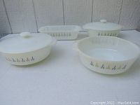 Front view of four Fire King Candle Glow milk glass bakeware pieces: two casseroles with lids, one casserole without lid, and one loaf pan. All show the floral Candle Glow pattern.