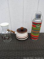 Photo showing three items: Plianfer France striped camping thermos, Anchor Hocking butterfly pattern juice carafe, vintage striped small saucepan with wooden handle.