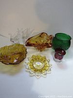 Full lot image showing 7 distinct vintage glass items including greenfish scale vase, amber ashtray, red glass souvenir pitcher, amber bowl and plate, and clear glass birds/statuettes.