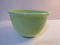 Side view of round vintage jadeite green milk glass mixing bowl with smooth opaque light green finish.