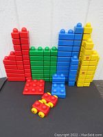 Side view of stacked red, green, blue, yellow LEGO Primo blocks with two red cars in front