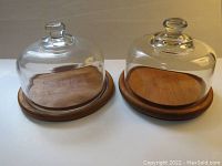 Pair of vintage teak wood and glass serving cheese domes, showing the difference in knob design and base style.