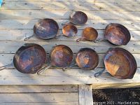 All nine cast iron pans arranged on wooden surface showing rust and size variation.