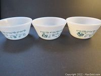 Three white milk glass bowls with green Kitchen Aids pattern on side, shown side by side.
