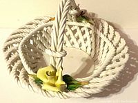 White ceramic basket with woven texture and twisted handle. Hand painted yellow flowers with green leaves on the exterior and handle base.