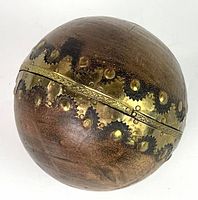 Top view of the antique wood baseball with brass and riveted gear-like adornments around the middle, showing the brown wood surface and metallic band.