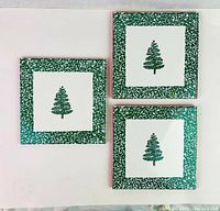 Set of three square ceramic tiles painted with Christmas tree and green speckled borders.