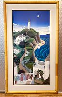 Framed art print showing vertical coastal scene with lighthouse, houses on cliffs, ocean waves, and moonlit sky. Enclosed behind glass in bamboo frame.