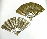 Pair of vintage brass decorative fans with detailed embossed dragon patterns, laid flat on white surface showing full design and fan structure.