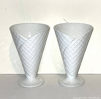 Two white porcelain vases side by side showing waffle pattern and pedestal base