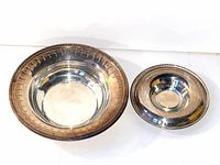 Photo showing two silver plated bowls side by side on a white surface, larger bowl with etched decorative rim and smaller plain bowl.