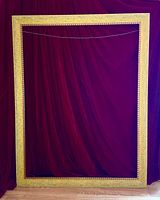Full view of the large rectangular picture frame against a dark red fabric background showing its burnished tan wood and gold finish.