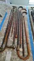 Seven vintage wooden walking canes laid out on patterned fabric, showing variations in handle style and wood finish.
