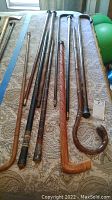 Overview photo showing nine vintage wooden canes of various styles and finishes laid out on patterned fabric.