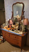 Full view of antique tiger oak dresser with shaped beveled mirror in a bedroom setting showing dresser top with various decorative items.