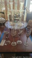 Photo of the cake stand with four stemware glasses and two white floral candle holders, arranged on a wooden table.