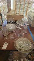 Full lot on wooden table with box behind, showing stemware, platters, candle holders, and sugar dish.