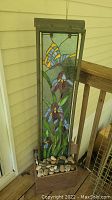 Full view of the tall water fountain with stained glass panel showing butterfly and flowers, wooden frame, and stone base.