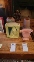 Front view of Hall pottery pieces on wood table including planter with bunny motif, vase with embossed leaves, pink pedestal planter, and other items.