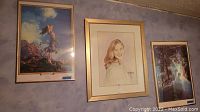 Three framed pictures hanging on a wall: two Maxfield Parrish prints and one portrait of a young woman.