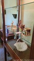 Glass shelves holding ceramic deer planters, white glass basket, books, and bookend
