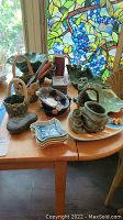 Photo of various vintage handcrafted pottery and novelty tableware including frog-themed ceramics on a wooden table near window