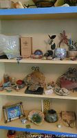 Photo showing multiple shelves with stone art, glass crystals, decorative sculptures, bowls, figurines, and framed picture.