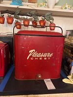 Front view of red vintage metal cooler with 'Pleasure Chest' logo and metal handle on lid.