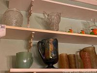 Shelf with various pitchers and textured drinking glasses, including an iridescent pitcher and a green ceramic mug.